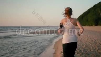 日落时分，在海上海岸的海滩上跑步的女人带着电话的背面景色